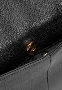 Zwart leren handtas interieur met een tekstuurafwerking, een gouden drukknoopsluiting en een contrasterende donkere stoffen voering.