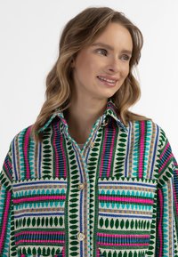 Camicia a fantasia colorata in verde, rosa, blu e bianco con colletto, bottoni dorati e taschino sul petto con disegni geometrici.