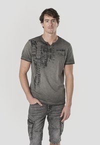 Gray T-shirt with a textured, faded design and graphic prints on the front; paired with gray cargo shorts featuring multiple pockets.