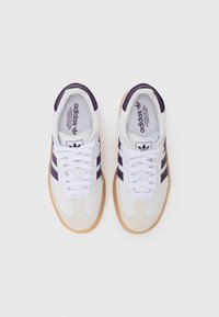 White athletic shoes with purple stripes, suede accents, white laces, and a gum rubber sole. Minimalistic design and padded collar.