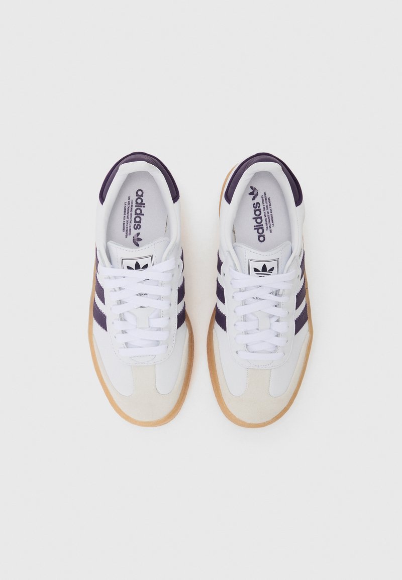 Scarpe atletiche bianche con strisce viola, dettagli in camoscio, lacci bianchi e suola in gomma naturale. Design minimalista con collo imbottito.