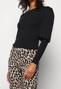 Top de punto negro con canalé y manga abullonada, combinado con pantalones beige que presentan un audaz patrón de leopardo negro.