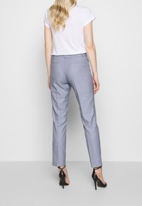 Grijze geruite op maat gemaakte broek met een slim fit, voorzien van zijzakken en een gladde textuur, gecombineerd met zwarte hoge hakken.