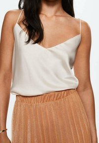 Hvid silke cami med V-hals og tynde stropper, parret med en plisseret, skinnende rosegul nederdel med elastisk talje.