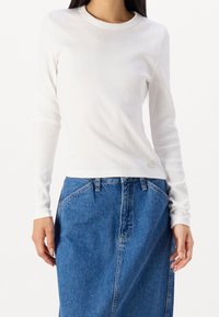 Vit långärmad ribbad topp med rund hals, i kombination med en högmidjad blå denimkjol med framfickor och en avslappnad passform.