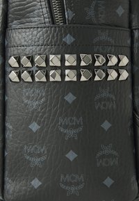 Zwarte leren tas met een gestructureerd oppervlak, voorzien van een reliëfpatroon en zilveren studs in een rij als decoratieve accenten.