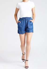 Shorts de mezclilla con cintura elástica, dos bolsillos laterales y un corte holgado. Combinados con una camiseta blanca básica y sandalias negras de tiras.