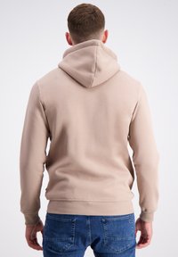 Šviesiai ruda gobtuvinė palaidinė, laisvo kirpimo, su gumbuotomis rankovėmis ir apatine dalimi, turi glotnų paviršių. Savybė yra didelis gobtuvas ir minimalistinis dizainas.