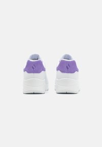 Zapatillas blancas con una lengüeta de talón de ante púrpura, suela de goma texturizada y parte superior sintética suave. La vista trasera muestra el detalle del logo en el talón.