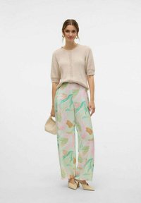 Cardigan beige a coste a maniche corte con bottoni abbinato a pantaloni ampi in tessuto leggero con fantasia pastello e scarpe beige con punta a punta.