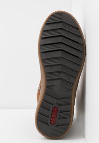 Brown shoe sole with a textured black rubber surface, featuring a zigzag tread pattern and a red logo. Sturdy design with visible size markings.