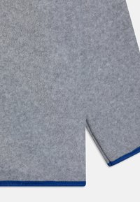 Grau gefertigtes Stoffkleidungsstück mit einer glatten Textur, das blaue Einfassungen entlang der Ränder aufweist und einen lockeren, leicht taillierten Schnitt hat.