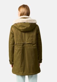 Parka verde oliva con capucha forrada de piel sintética, puños ajustables y detalle de botones en la parte frontal. La tela parece suave con un ligero brillo.