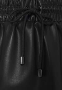 Pantaloni neri in pelle con coulisse, caratterizzati da una vita arricciata, cordino nero regolabile e dettagli metallici alle estremità del cordino. Texture liscia.