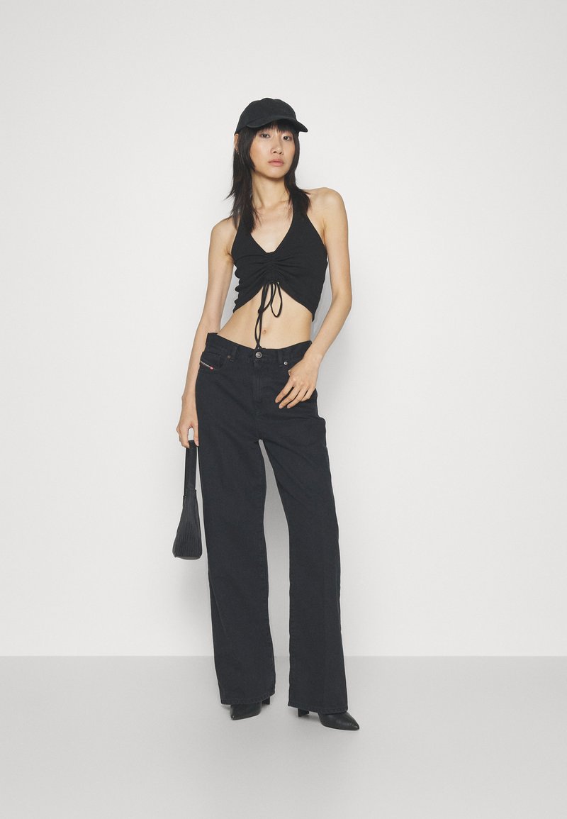 Schwarzes Crop-Top mit einer gerafften Vorderseite, kombiniert mit hochgeschnittenen schwarzen weit geschnittenen Jeans. Die Accessoires bestehen aus einer kleinen schwarzen Tasche und einer Kappe.