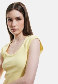 Top a righe giallo chiaro con scollatura rotonda e maniche corte a campana. Tessuto morbido, design aderente.