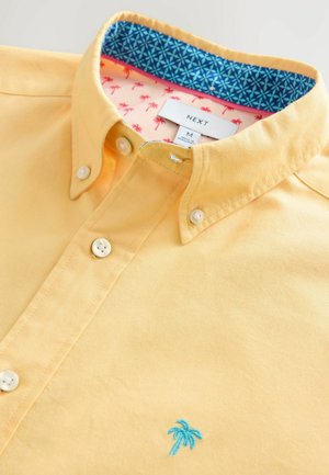 Gul skjorte med knapper og blå palmebroderi, udstyret med en kontrastfarvet krave indeni i blå og pink mønster samt to forreste knapper.