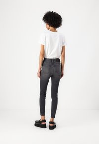 Černé skinny džíny s vysokým pasem, s hladkou denimovou texturou a dvěma zadními kapsami, doplněné o jednoduché bílé tričko a černou obuv.