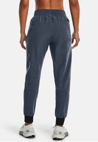 Man wearing navy blue jogger pants and white sneakers standing with back visible on white background.