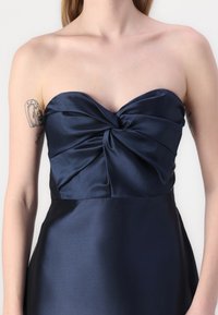 Námornícky strapless šaty s detailom skrúteného korzetu, hladkým saténovým povrchom a priliehavou siluetou. Doplnené štruktúrovaným pásom.