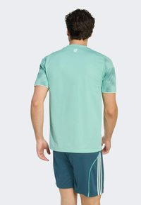 Ljust tealfärgad atletisk kortärmad tröja med rund halsringning, slät textur och subtil logotypdetalj på ryggen. Kombinerad med mörk teal shorts.