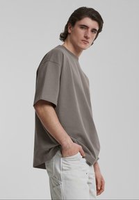 Camiseta de algodón gris de gran tamaño con mangas cortas, cuello redondo y un sutil detalle de logo. Combinada con pantalones blancos con múltiples bolsillos.