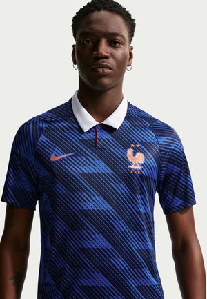 Man draagt een blauw Frans voetbalshirt met witte kraag, diagonale strepen, Nike-logo en een tweesterren hansembleem op de borst, neutrale achtergrond.