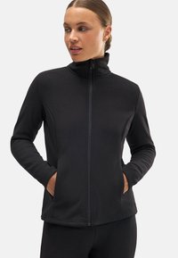 Chaqueta negra con cremallera y cuello alto, mangas largas y bolsillos laterales. Tejido suave con un diseño ajustado y mínimos detalles de costura.