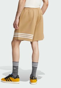 Brown shorts feature white stripes at the hem. Worn with gray striped socks and black sneakers with yellow accents. Visible pocket at the back.