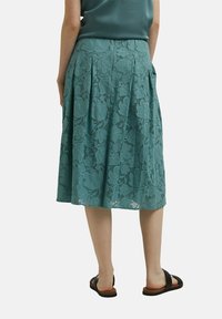 Falda de encaje verde azulado con patrón floral, diseño plisado, hasta la rodilla, con una cinturilla suave, combinada con sandalias negras.