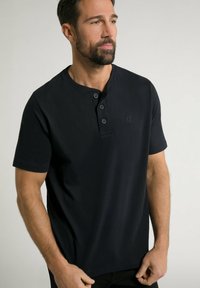 Černé krátké rukávy henley tričko vyrobené z bavlny, s 2knoflíkovou légou a malým embosovaným logem na prsou. Hladká textura.