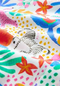 Buntes Baumwollgewebe mit markanten Mustern, die tropische Blumen, einen pinken Leoparden und lebendige Vögel auf weißem Hintergrund zeigen.