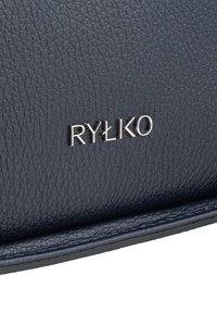 Navy blue teksturowany skórzany akcesorium z tłoczonym srebrnym logo "RYŁKO". Posiada gładką krawędź i subtelny połysk.