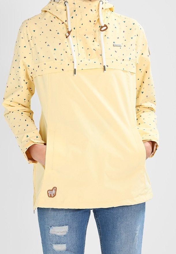 Gul anorak med ett tryckt mönster av små färgade trianglar, justerbar huva med dragsnören och framficka. Har en brun logotypapplikation.