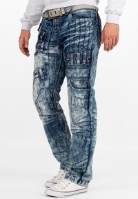 Pantaloni cargo in denim blu con finitura sbiadita e usurata. Presentano molteplici tasche, borchie decorative e accenti cuciti.
