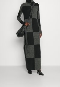 Lång tröjdress i ett rutmönster av mörkgrått och svart. Mjuk ullblandning, med hög krage och långa ärmar. Bärs med en svart väska.