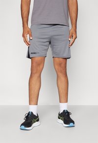 Lichtgrijze sportshorts met zwarte accenten, logo op de linkerdij, gecombineerd met zwarte sneakers en witte enkelsokken.