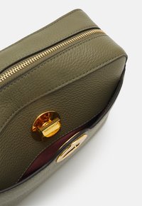 Borsa in pelle verde oliva con cerniera e hardware dorati. Presenta una texture liscia e una fodera interna bordeaux. Accento del logo rotondo visibile.