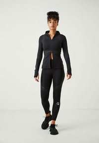 Black athletic jacket with a zip front, paired with fitted black leggings. The outfit features textured fabric and a logo on the leg.