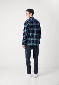 Camisa de cuadros en azul marino y verde con mangas largas, cuello abotonado y corte relajado, combinada con jeans oscuros y zapatillas blancas.