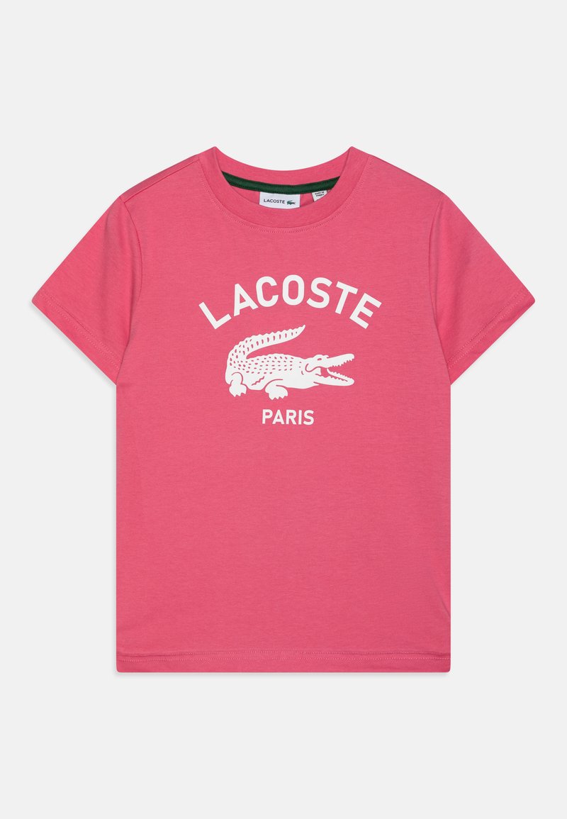 Różowa bawełniana koszulka z białym logo krokodyla i napisem "LACOSTE PARIS" w łuku. Krótkie rękawy i okrągły dekolt.
