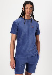 T-shirt à manches courtes en velours côtelé bleu et shorts assortis, présentant des rayures horizontales et un petit logo sur la poitrine, avec une texture douce.