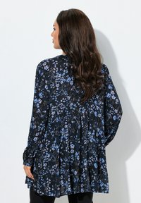 Blouse noire à motif floral avec des fleurs bleues et blanches, manches longues et dos plissé pour plus de texture.