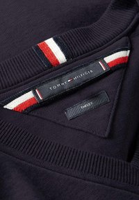 Granatowy sweter z prążkowaną fakturą, posiadający czerwone, białe i niebieskie paski na kołnierzu. Metki zawierają "TOMMY HILFIGER" i "THFLEX."
