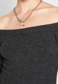 Silberne Kettenhalskette mit großen Gliedern und einem zentralen Anhänger mit rosa floralen Akzenten und Strasssteinen, getragen über einem anthrazitfarbenen Pullover.