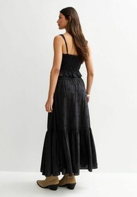 Top nero a peplo con corpetto arricciato abbinato a una lunga gonna nera a più strati, con motivi floreali testurizzati e design lungo fino alla caviglia.
