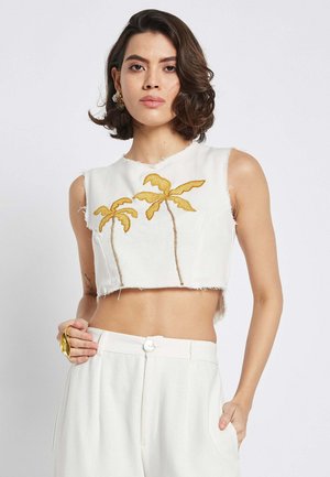 Weißes, gekürztes Oberteil mit fransigen Kanten und gelben, gestickten Palmen. Das Model trägt weiße High-Waist-Hosen und hält einen goldenen Ring.