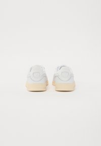 Baskets blanches avec une tige en cuir lisse, doublure textile douce et semelle en caoutchouc beige. Présente des talons arrondis et des accents texturés.