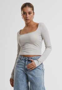 Lys grå langermet topp med firkantet hals, laget av strukturert stoff med en subtil glans, kombinert med høyt liv blå jeans.