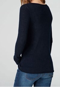 Mörkblå stickad tröja med långa ärmar, rund halsringning och mjuk textur. Bärs tillsammans med blå jeans, vilket framhäver en avslappnad passform och stil.